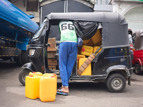 Worker Fills Auto Rickshaw With Yellow Containers at Market