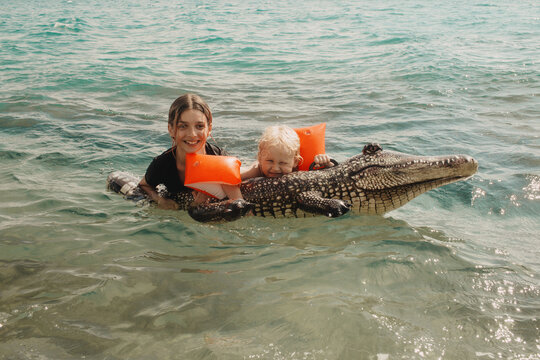 The children are swimming in the water with an inflatable crocodile