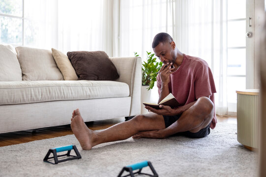 Man reading book on floor with exercise equipment nearby.
