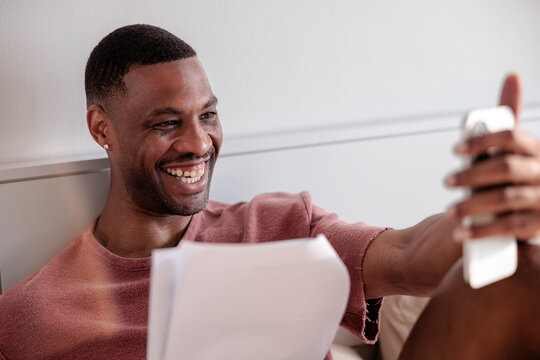 Man smiles while video chatting and holding papers.