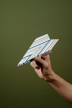 a striped paper airplane is held by a man against green backdrop
