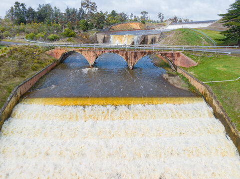 Arched road bridge crossing water rushing over a reservoir spillway