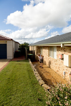 Elderly man pressure washing concrete blocks in yard under blue sky