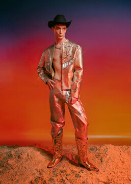 Man in a cowboy outfit and cowboy hat standing on sandy ground