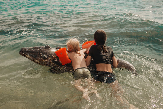 The children are swimming in the water with an inflatable crocodile