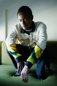 Lifestyle portrait of a man crouching on a green sofa indoors