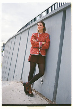 Woman stands confidently against a gray wall in urban setting