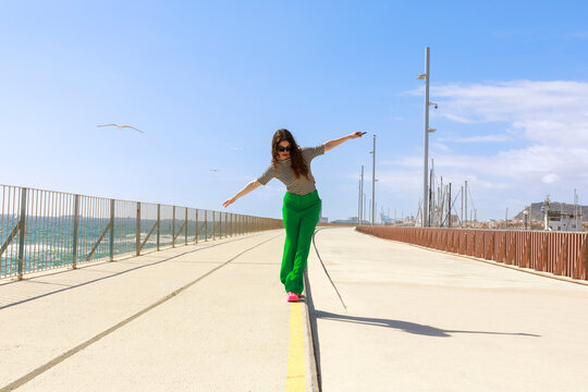 Woman Balances on a Line Along a Seaside Walkway 