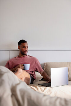 Man in bed with coffee and laptop.