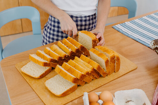 Unknown woman wearing sleepwear cutting a loaf into pieces