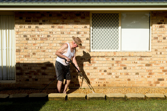 Elderly man pressure washing concrete blocks beside brick house