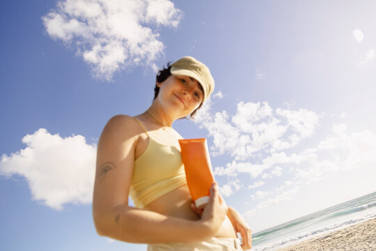 Woman holding sunscreen under blue sky at beach