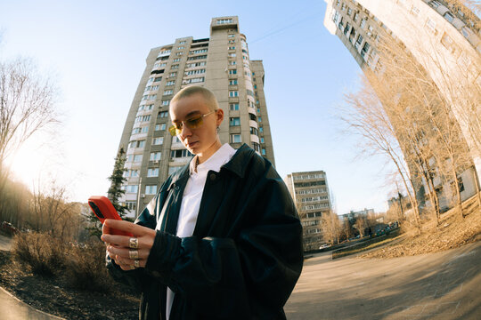 Person Checks Phone Near Tall Buildings During the Day