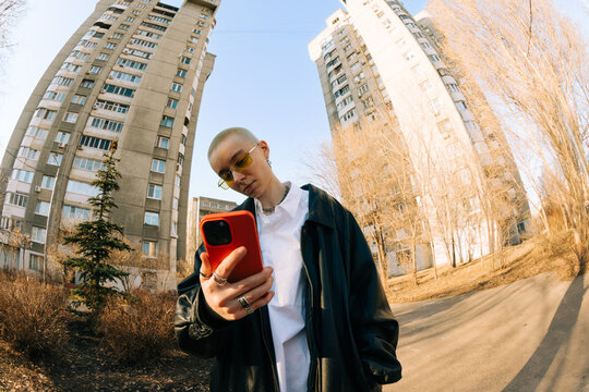 Young Person Checks Phone Near Tall Buildings in the City