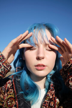 Young person with blue hair poses under clear sky