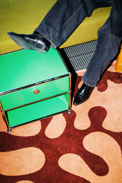 Man flashes black shoes while resting foot on green cabinet