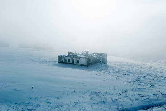 Abandoned house in snowy foggy field