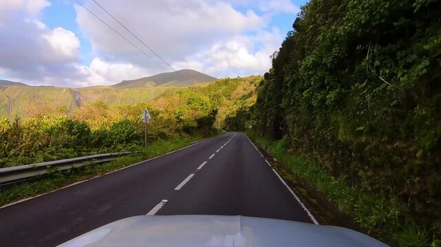 Scenic car point of view drive along mountain road with sunset waterfalls and lush volcanic cliffs near Poco da Ribeira do Ferreiro in the Azores Portugal