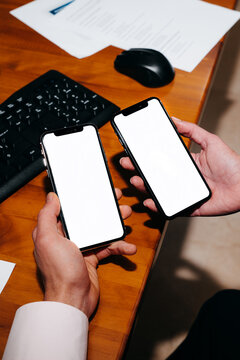 Two Hands Holding Smartphones With White Screen on the Desk