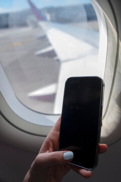 Airplane window and mobile phone in hand closeup