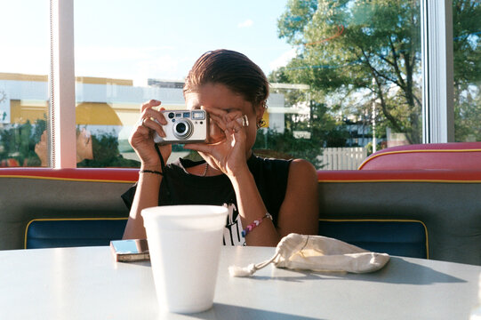 Young Woman Using Film Camera in Diner Booth with Coffee