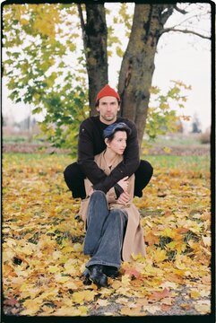 A couple enjoys autumn sitting by a tree surrounded by leaves.