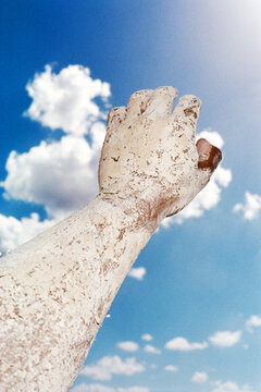 Hand covered in white clay reaching towards the blue sky.