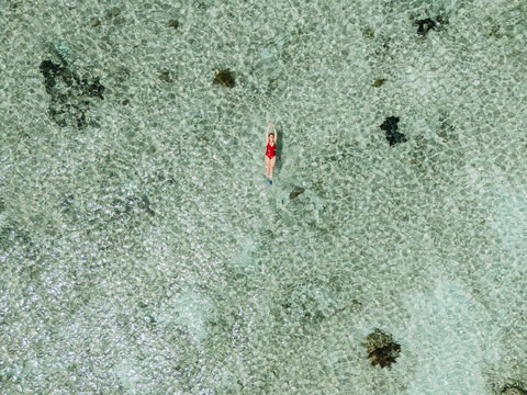 Aerial view of woman floating in shallow tropical lagoon
