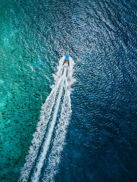 Aerial view of boat crossing turquoise and deep blue water
