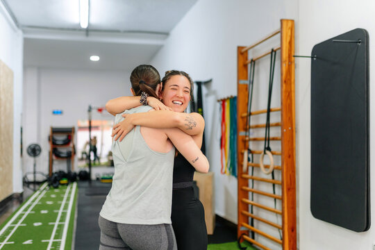 Female personal trainer hugging happy athlete in gym