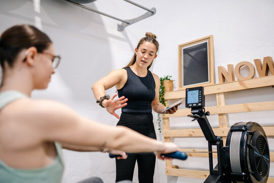 Personal trainer guiding woman during rowing machine workout