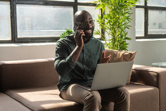 Smiling Black Man Talking on Phone While Working on Laptop