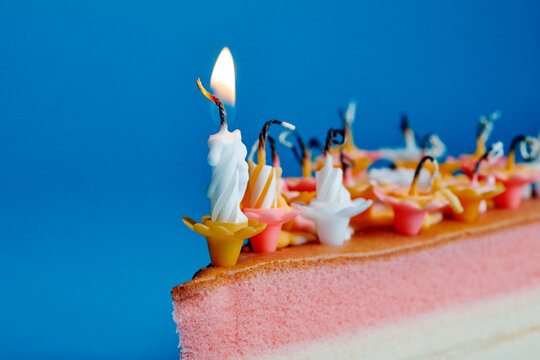 a row of birthday candles on a cake slice with one flame still burning
