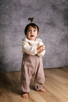 Curious baby girl standing looking up clapping hands