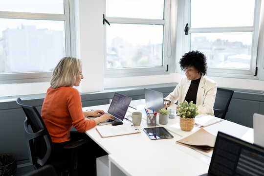 Businesswomen collaborating on laptops in modern office