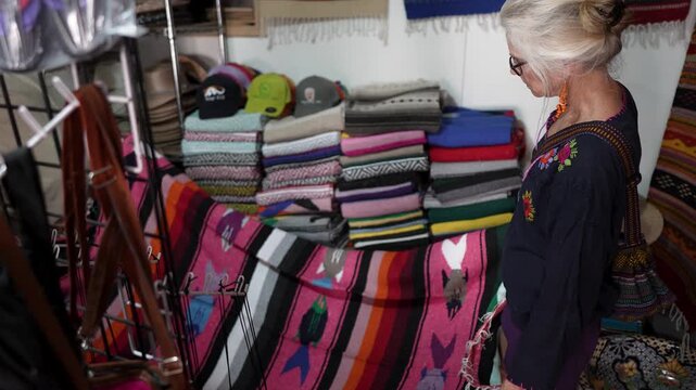 Senior woman explores a shop in Mulege Baja California Sur Mexico while looking at colorful blankets and local items.