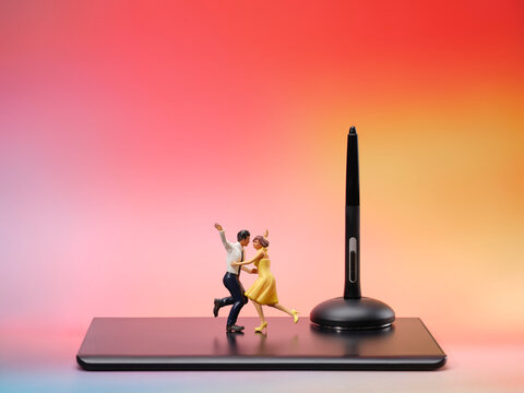 Miniature couple dancing on a tablet with a stylus stand