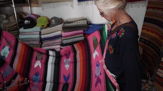 Senior woman browses textiles while shopping in a tourist shop in Mulege, Baja California Sur Mexico during her trip.