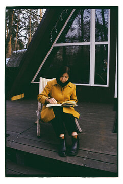 A woman draws in a sketchbook on the street near a house.