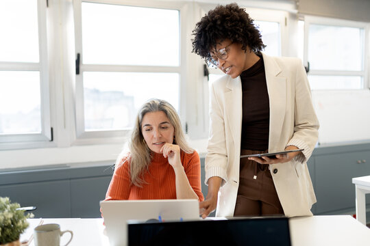 Businesswomen collaborating on laptop in modern office