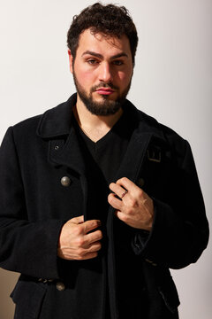Man in black coat stands against white background