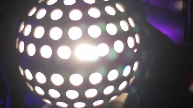 A visualization of a rotating disco ball light emitting bright light in a dark room. This stage light creates a lens flare effect and intense white flashes of light (strobe effect).