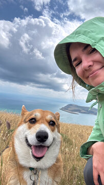 Woman hiking with corgi dog taking selfie on coastal cliff trail