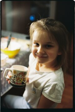 A little girl with a cup in her hands is sitting at a table.