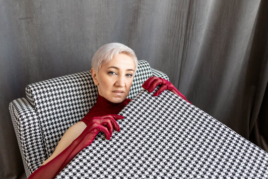 A woman sits on a chair with a pillow on her lap.