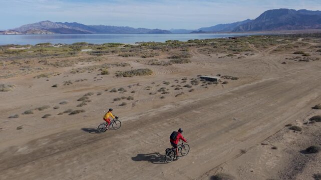 Mature man and woman ride bikes through desert terrain near La Gringa at Bahia De Los Angeles by the Sea of Cortez in Baja California, Mexico.