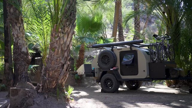 Teardrop camper trailer is parked in a desert oasis among palm trees in San Ignacio Baja California Sur Mexico during early morning.