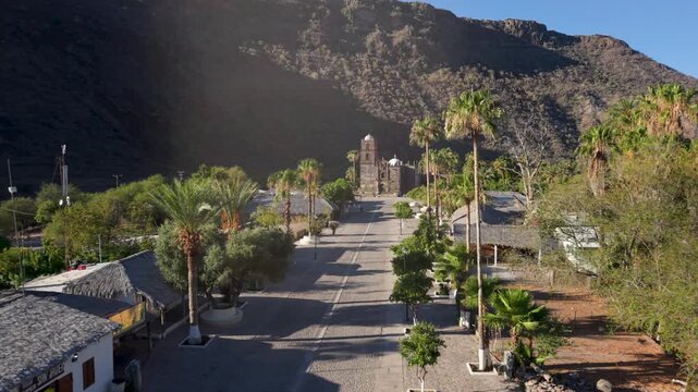 View beautiful aerial shots of San Javier Mission and the town at sunrise, showcasing palm trees and landscape in Baja California Sur., Mexico