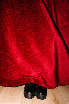 Black shoes behind red velvet curtain