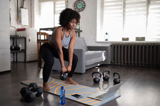 Black sportswoman lifting kettlebell during online training